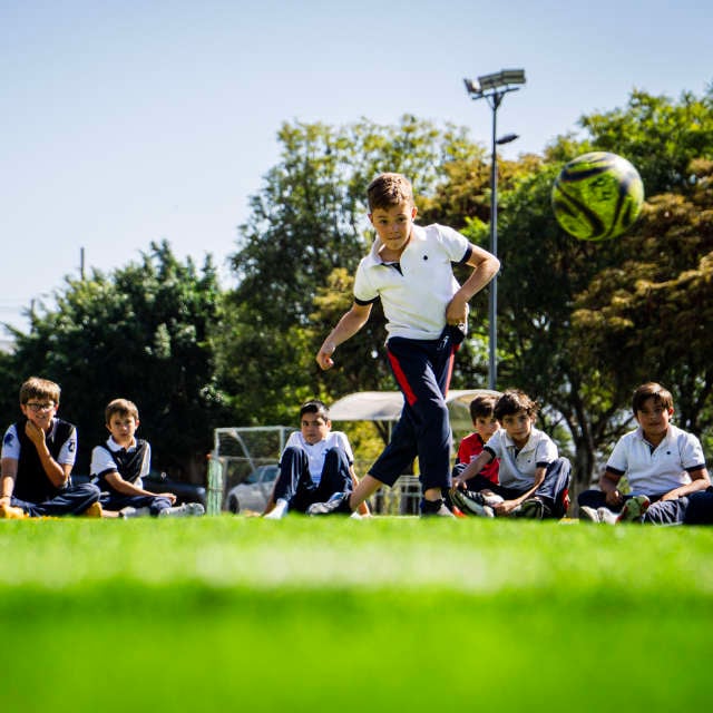 Niños de primaria en clase de deportes practicando futbol