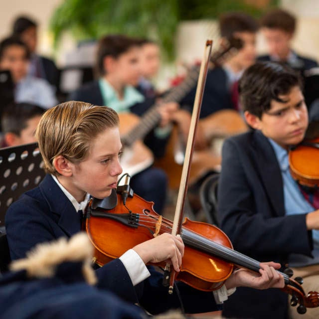 Niño tocando el violin con a Orequesta Álamos