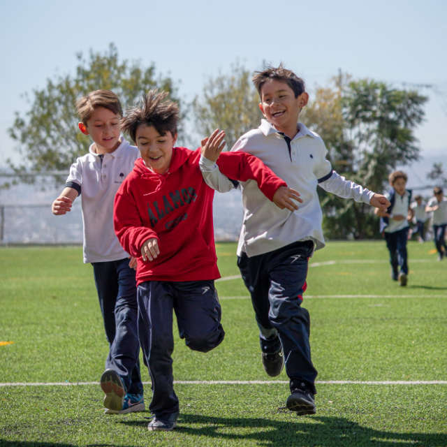 Niños de primaria corriendo felices en la cancha de futbol del Colegio Álamos